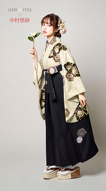 黒い花の模様をあしらったベージュの着物と赤紫の袴を着たモデル
